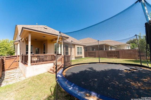 rear view of property with a trampoline, a yard, and a wooden deck