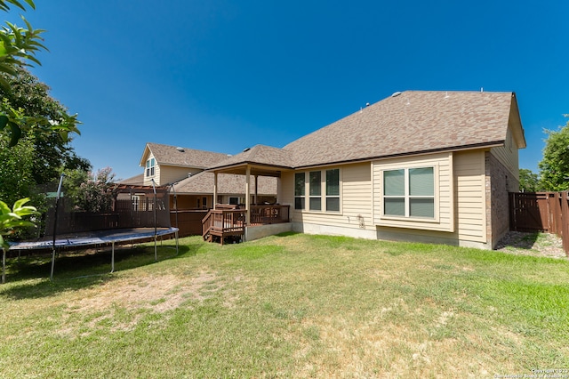 back of house featuring a wooden deck, a trampoline, and a lawn