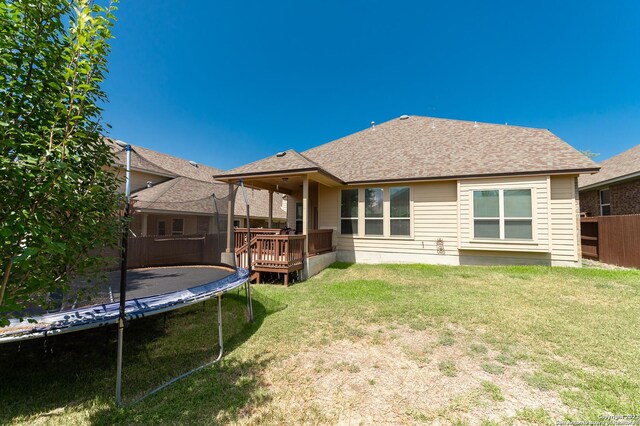 back of house with a deck, a lawn, and a trampoline