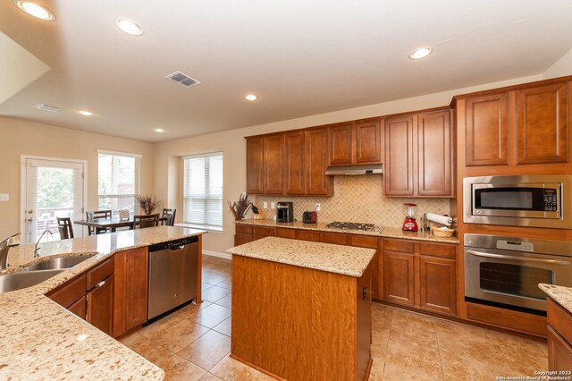 kitchen with light tile patterned floors, light stone countertops, a kitchen island, and stainless steel appliances