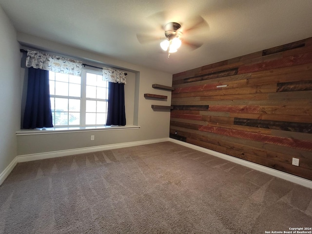 carpeted spare room featuring wood walls and ceiling fan