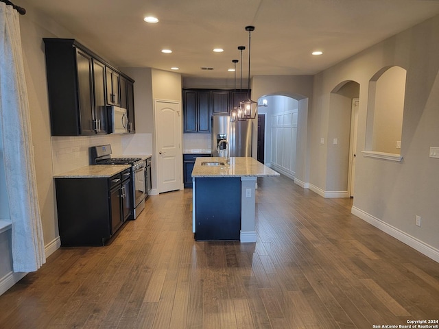 kitchen with light stone countertops, backsplash, stainless steel appliances, and a kitchen island with sink