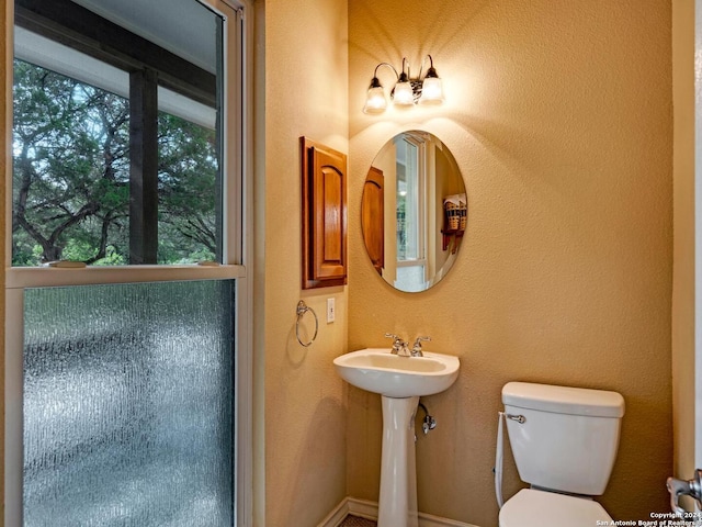 half bath with a textured wall, a sink, and toilet