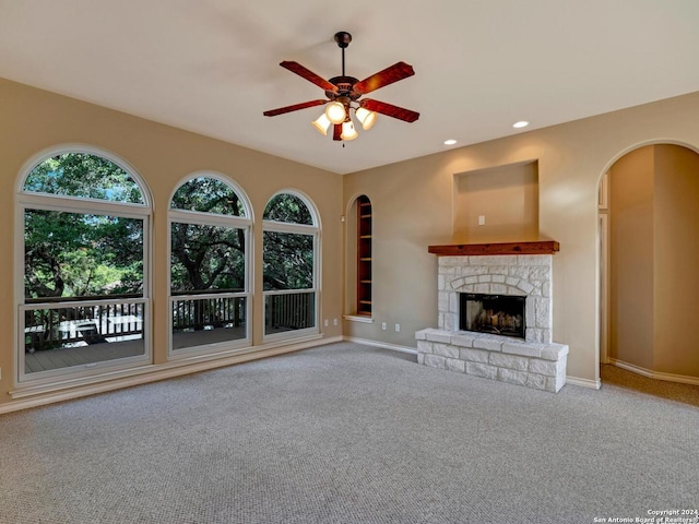 unfurnished living room with carpet floors, arched walkways, ceiling fan, and a stone fireplace