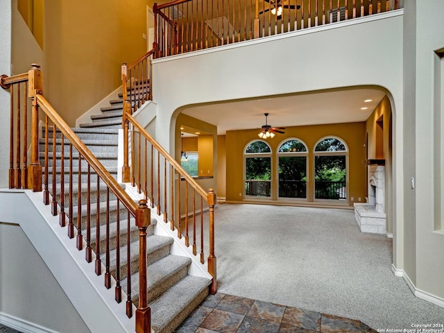 stairway with arched walkways, baseboards, carpet flooring, and a high ceiling