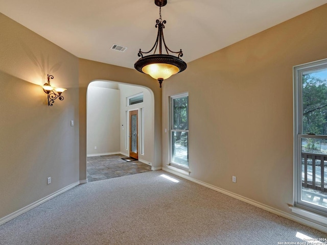 empty room featuring a healthy amount of sunlight, visible vents, arched walkways, and carpet flooring