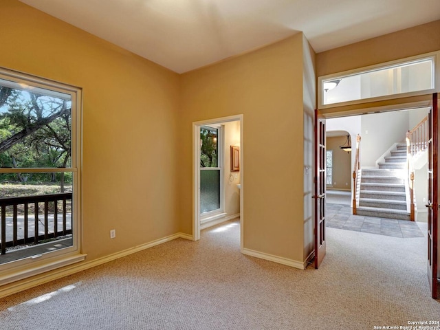 spare room featuring light carpet, stairs, baseboards, and arched walkways