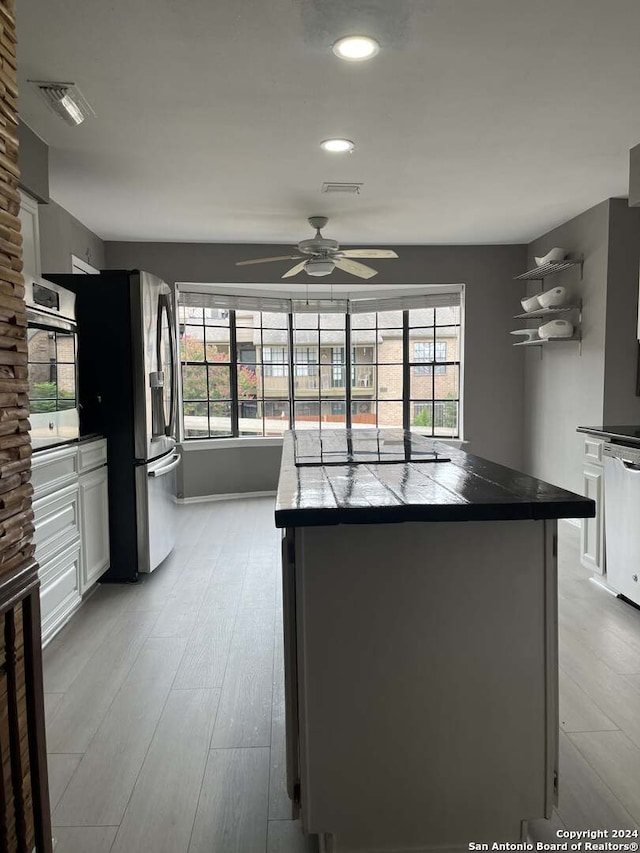 kitchen featuring light hardwood / wood-style flooring, white cabinets, ceiling fan, appliances with stainless steel finishes, and tile countertops