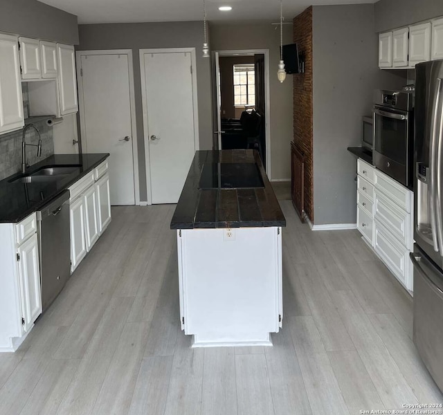 kitchen featuring appliances with stainless steel finishes, white cabinetry, hanging light fixtures, and light hardwood / wood-style floors