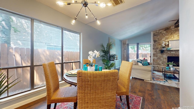 dining area featuring lofted ceiling, a notable chandelier, a stone fireplace, and dark hardwood / wood-style flooring