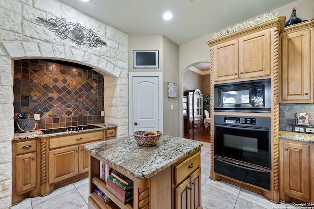 kitchen with light tile patterned flooring, tasteful backsplash, light stone counters, a kitchen island, and black appliances