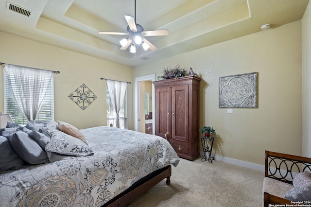 bedroom with light carpet, a raised ceiling, multiple windows, and ceiling fan