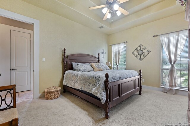 carpeted bedroom with ceiling fan and a raised ceiling