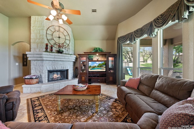 living room with light tile patterned flooring, a stone fireplace, lofted ceiling, and ceiling fan