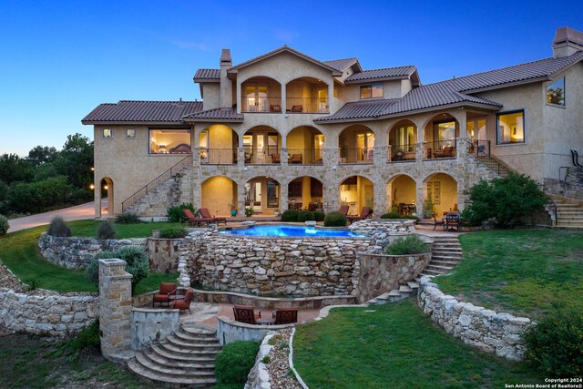 back house at dusk featuring a balcony and a patio area