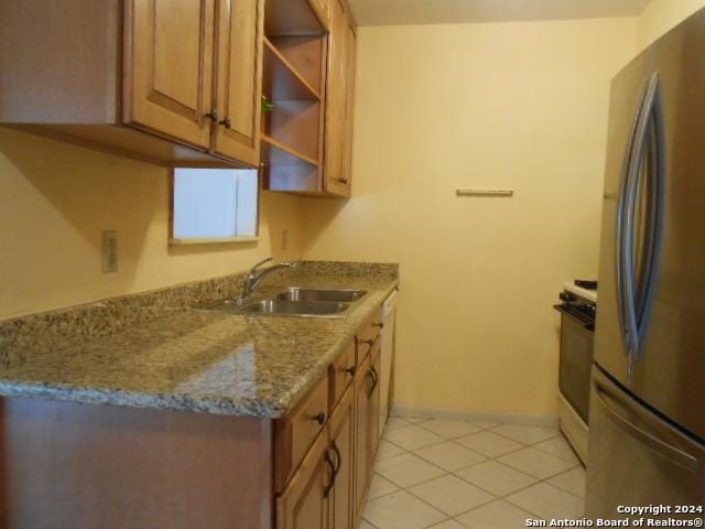 kitchen with light tile patterned flooring, white range with electric stovetop, sink, stainless steel fridge, and light stone countertops