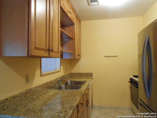 kitchen with stone counters, light tile patterned flooring, white range with electric stovetop, stainless steel refrigerator, and sink