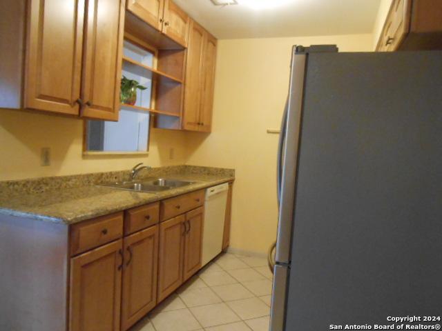 kitchen featuring sink, stainless steel fridge, white dishwasher, light stone countertops, and light tile patterned flooring