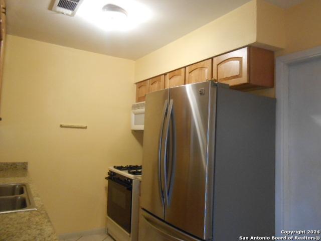 kitchen with light brown cabinetry, sink, and white appliances