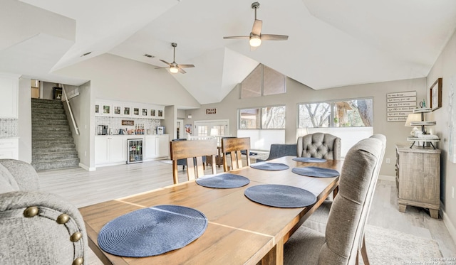 dining space featuring lofted ceiling, wine cooler, bar, ceiling fan, and light hardwood / wood-style flooring