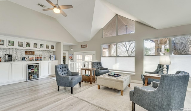 living room with high vaulted ceiling, light hardwood / wood-style floors, beverage cooler, french doors, and indoor bar