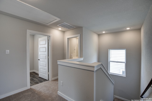 corridor featuring a textured ceiling and dark colored carpet