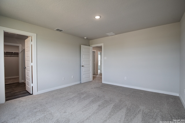 unfurnished bedroom with a textured ceiling, a closet, dark carpet, and a walk in closet