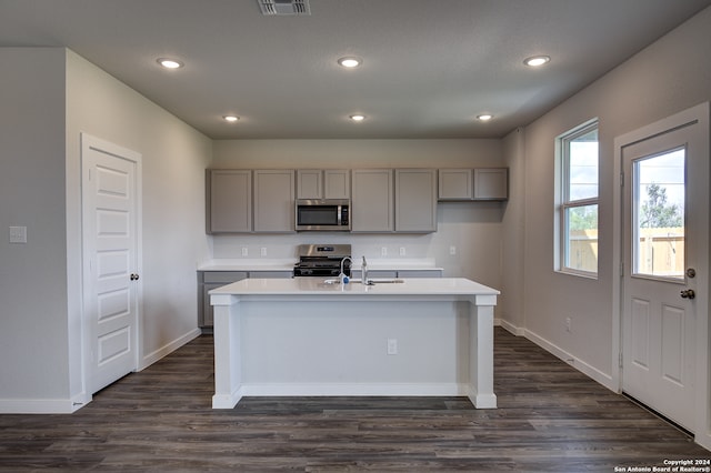 kitchen featuring dark hardwood / wood-style flooring, sink, appliances with stainless steel finishes, gray cabinetry, and a kitchen island with sink