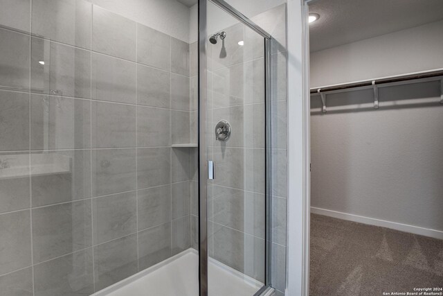 bathroom featuring a walk in closet, a shower stall, and baseboards