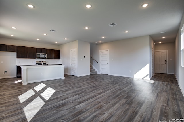 kitchen with dark brown cabinets, stainless steel appliances, a kitchen island with sink, and dark hardwood / wood-style floors