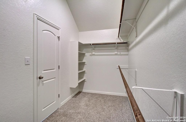 walk in closet with light colored carpet and vaulted ceiling