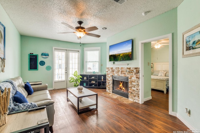 living room with ceiling fan, a fireplace, dark hardwood / wood-style flooring, and a textured ceiling