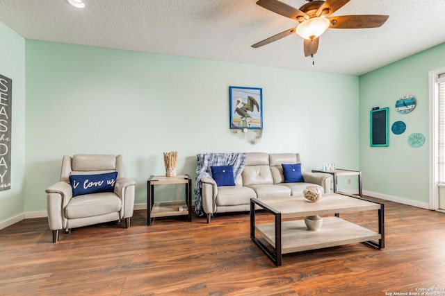 living room featuring dark wood-type flooring, ceiling fan, and a textured ceiling