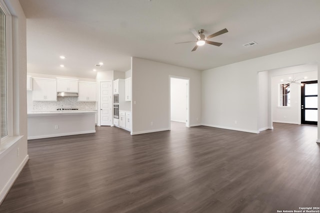 unfurnished living room featuring ceiling fan with notable chandelier and dark wood-type flooring