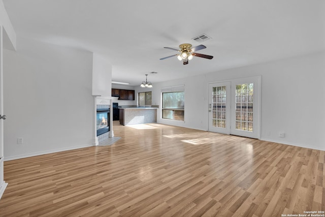 unfurnished living room with ceiling fan with notable chandelier and light hardwood / wood-style flooring