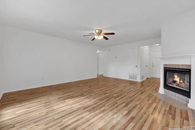 unfurnished living room with ceiling fan, a tiled fireplace, and light wood-type flooring