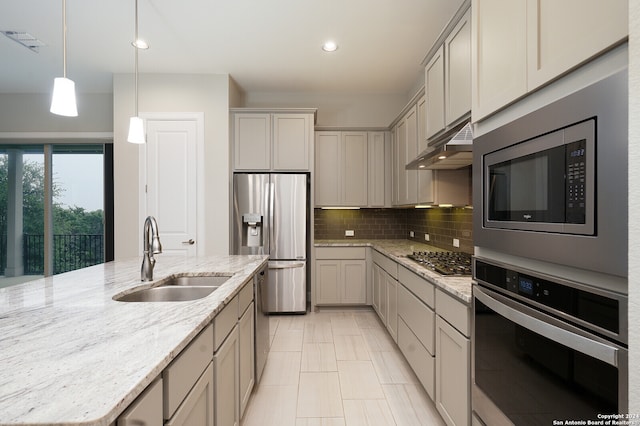 kitchen with stainless steel appliances, wall chimney range hood, sink, light stone counters, and decorative light fixtures