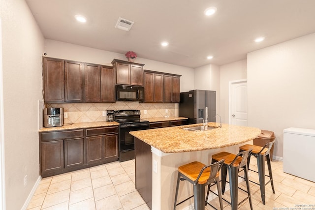 kitchen featuring dark brown cabinets, a kitchen breakfast bar, tasteful backsplash, black appliances, and a center island with sink