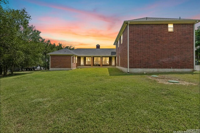 back house at dusk featuring a lawn