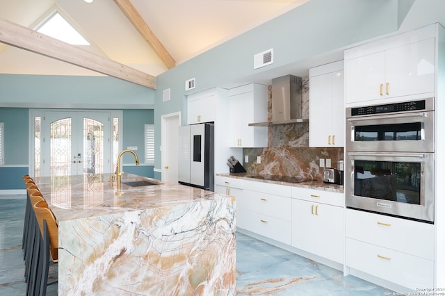 kitchen with beamed ceiling, white refrigerator, wall chimney range hood, sink, and stainless steel double oven