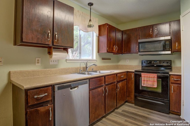 kitchen with decorative light fixtures, sink, stainless steel appliances, dark brown cabinets, and light wood-type flooring