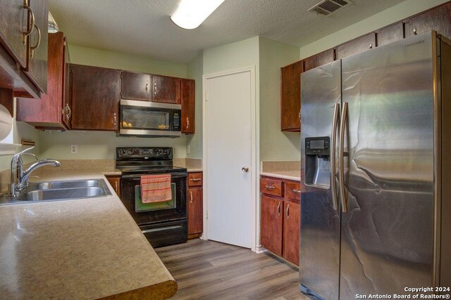 kitchen with appliances with stainless steel finishes, sink, a textured ceiling, and light hardwood / wood-style flooring