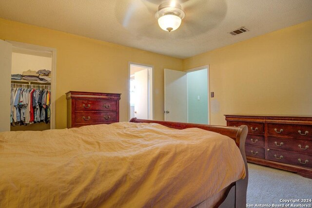 carpeted bedroom featuring a walk in closet, a closet, and ceiling fan