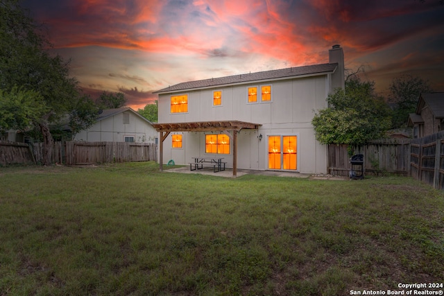 back house at dusk featuring a patio and a lawn