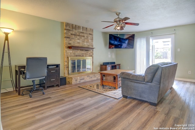 living room with ceiling fan, a textured ceiling, a brick fireplace, and wood-type flooring