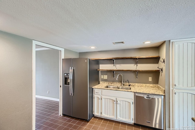 kitchen featuring sink, stainless steel appliances, light stone counters, white cabinets, and a textured ceiling