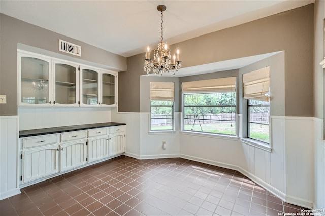 unfurnished dining area featuring dark tile patterned flooring and an inviting chandelier