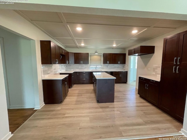 kitchen featuring light wood-type flooring, a sink, coffered ceiling, decorative backsplash, and baseboards
