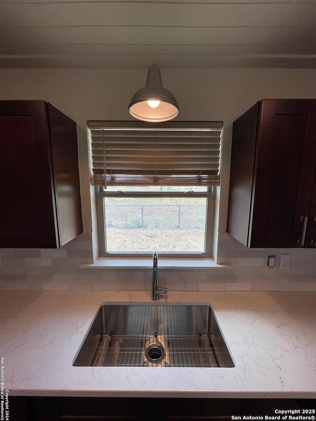 kitchen with dark brown cabinetry, decorative backsplash, light stone countertops, and a sink