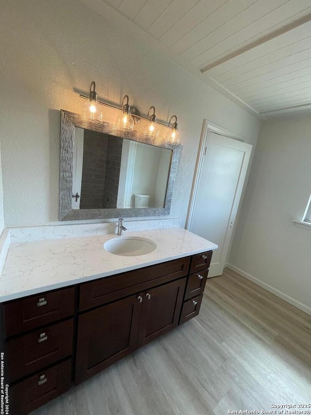 bathroom featuring toilet, wood finished floors, wooden ceiling, baseboards, and vanity